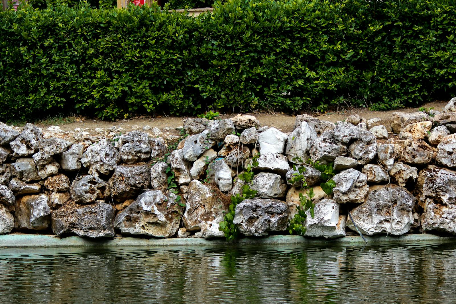 Tan stone retaining wall stepping down a sloped backyard with planted pockets.